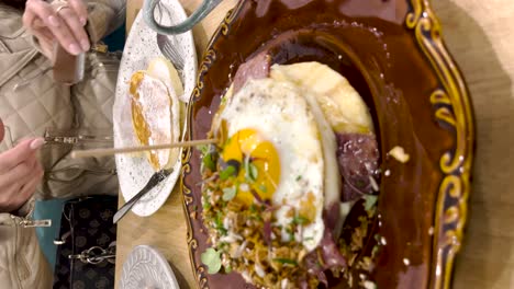 Vertical-view-of-a-gourmet-breakfast-sandwich-featuring-a-fried-egg-and-crispy-bacon-nestled-between-two-slices-of-bread,-with-a-side-of-chocolate-pancakes