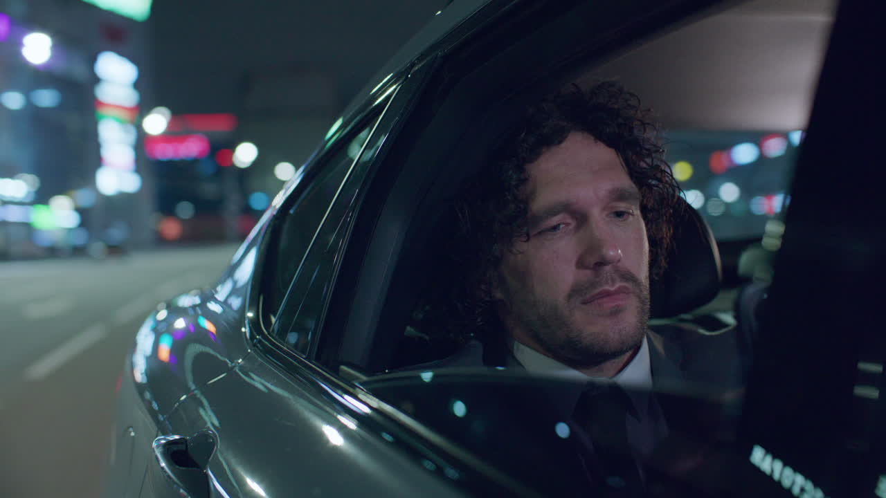 Empresario enviando mensajes de texto por teléfono mientras viaja en coche por la ciudad de noche