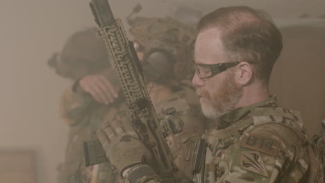 side view of soldiers in camouflage uniform and safety glasses testing shotgun indoors