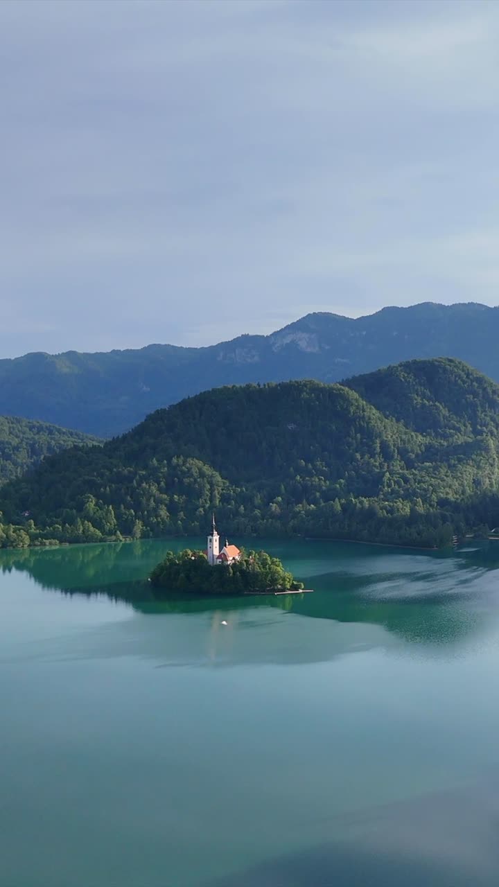 Scatto aereo verticale del Lago di Bled e della sua isola con la chiesa circondata da foreste lussureggianti.