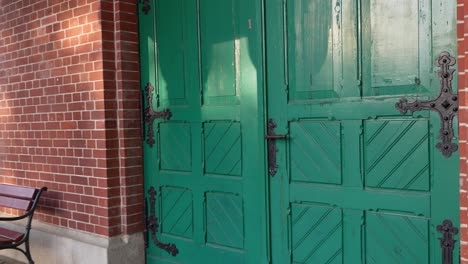 a wide view of old green wooden doors in a historic chapel in szczecin. benches stand in front of the red brick wall. subtle camera movement in soft daylight.