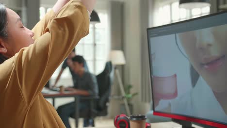 asian female digital editor stretching while works in photo editing software on her personal computer with big display in office