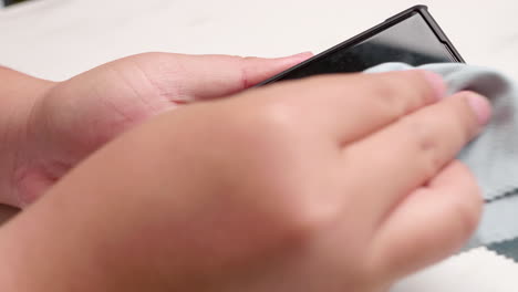 a close-up of an individual cleaning up the screen of her mobile smart phone using a microfiber cloth