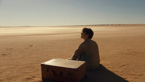 man sitting with a suitcase in a vast desert landscape