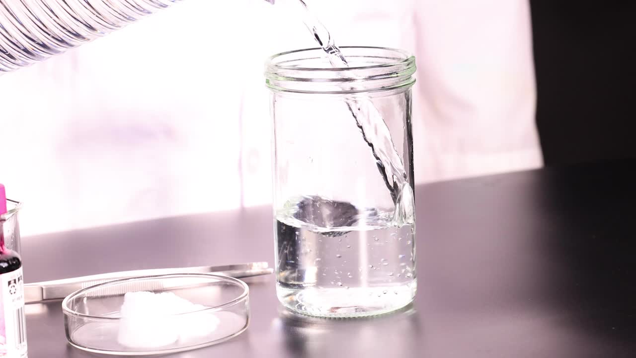 한 사람 이 실험실 테이블 에 있는 유리 항아리 에 액체를 부어 놓고, 근처 에 건조 한 얼음 이 있으며, 밝은 조명 아래 있다