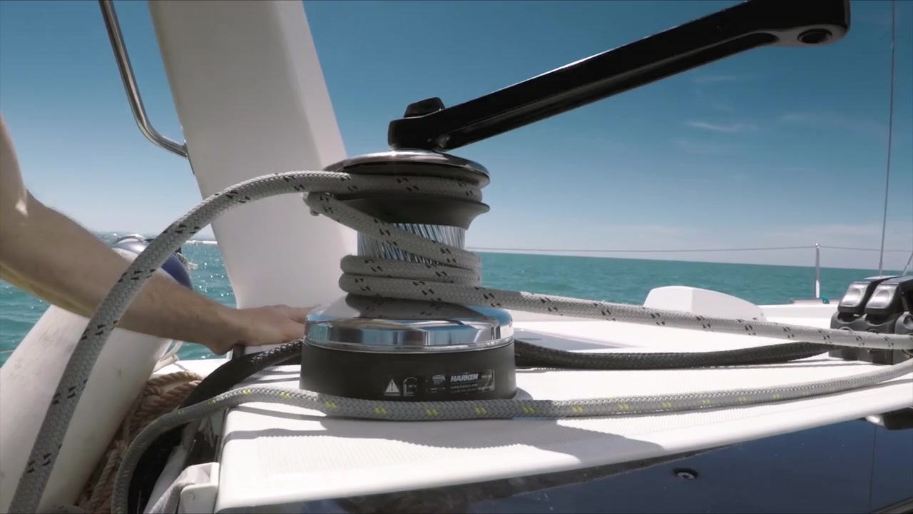 Primo piano di una mano che usa una manovella e un verricello per issare la vela su uno yacht.