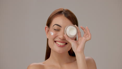 mujer sonriente sosteniendo crema para el cuidado de la piel