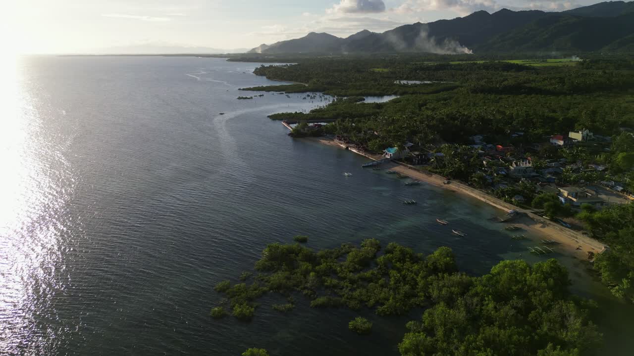 Stunning view of a lush tropical island village coastline facing picturesque cove during sunset at Catanduanes, Bicol, Philippines - aerial forward shot