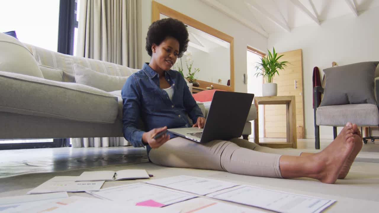 Happy african american woman sitting on floor, using laptop and working