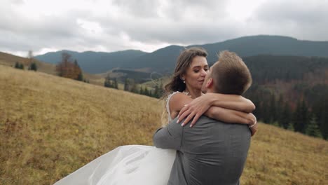 Lovely-young-newlyweds-bride-and-groom-embracing,-making-a-kiss-on-mountain-slope,-wedding-couple