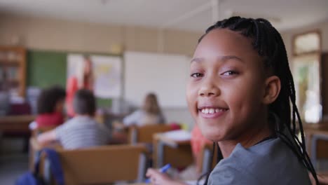 Mädchen-Lächelt,-Während-Sie-In-Der-Schule-Auf-Ihrem-Schreibtisch-Sitzt