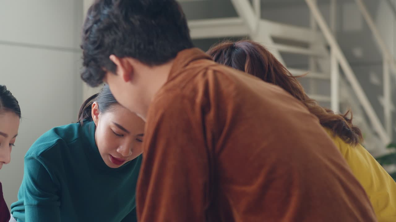 Asian businesspeople meeting brainstorming ideas about creative web design planning application and developing template layout for mobile phone project working together in small office.