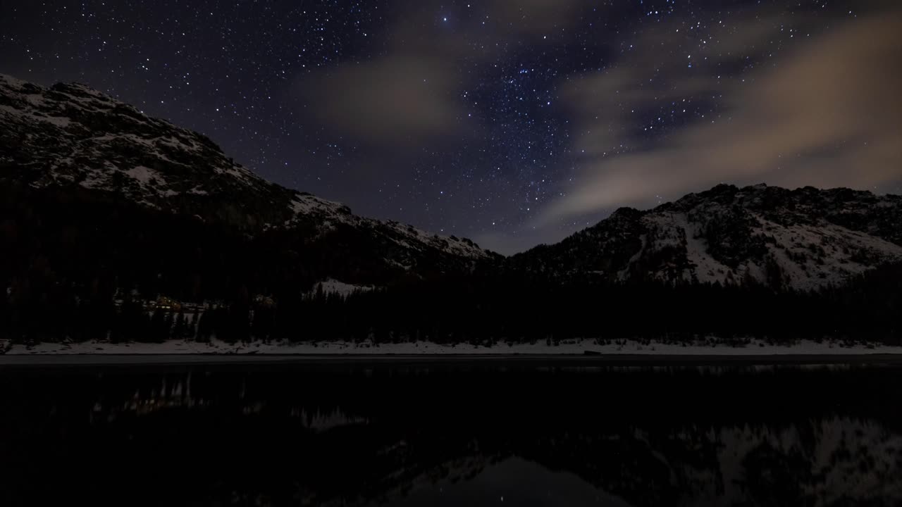 Nachthimmel-Zeitraffer mit schneebedeckten Bergen, die sich in einem Alpensee spiegeln, Italien.