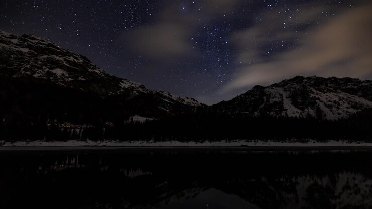 Nachthimmel-Zeitraffer mit schneebedeckten Bergen, die sich in einem Alpensee spiegeln, Italien.