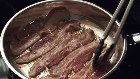 bacon frying in pan tended being tended by a chef