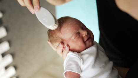 brushing the hair to a tiny sleeping newborn. female hands hold the baby and male hand uses a hairbrush.