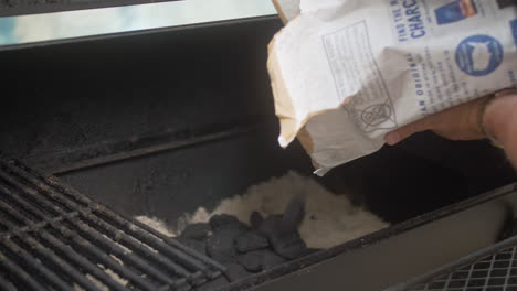 man pours bbq charcoal briquettes in to smoker from bag