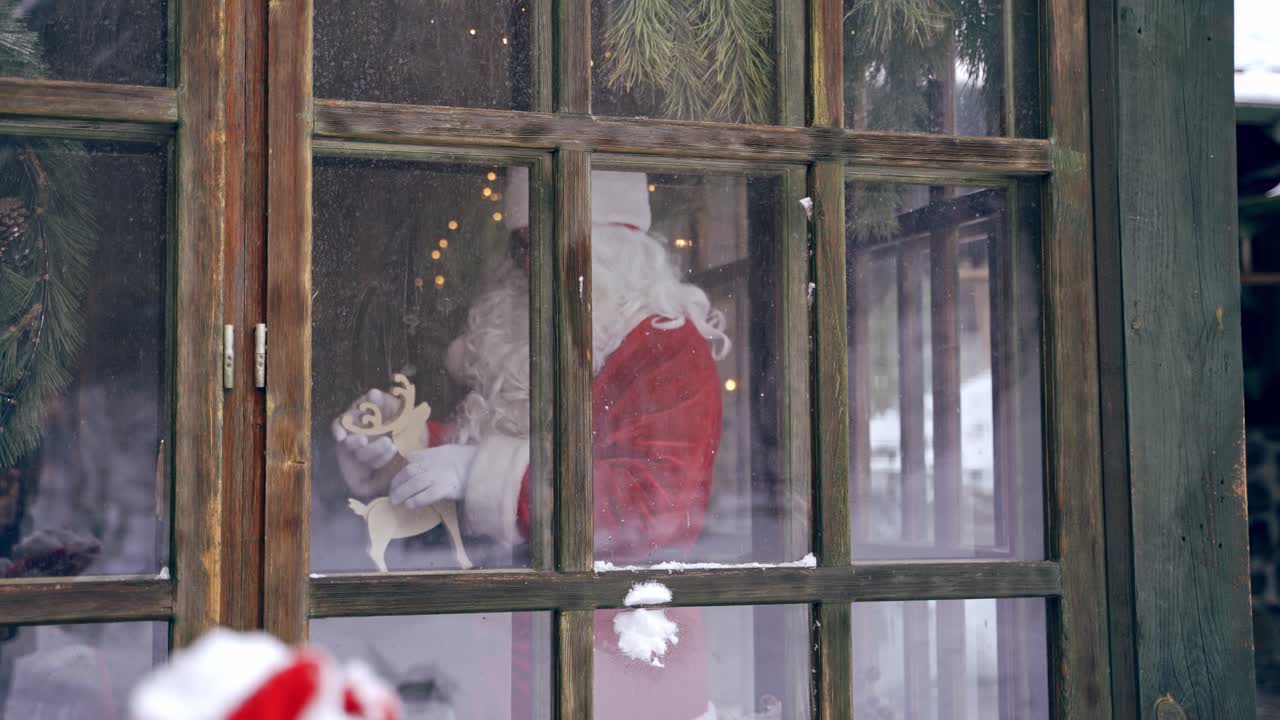 Santa Claus looking through the window. Snowball flying on the window. View from outdoors into the house with Santa. Xmas time.