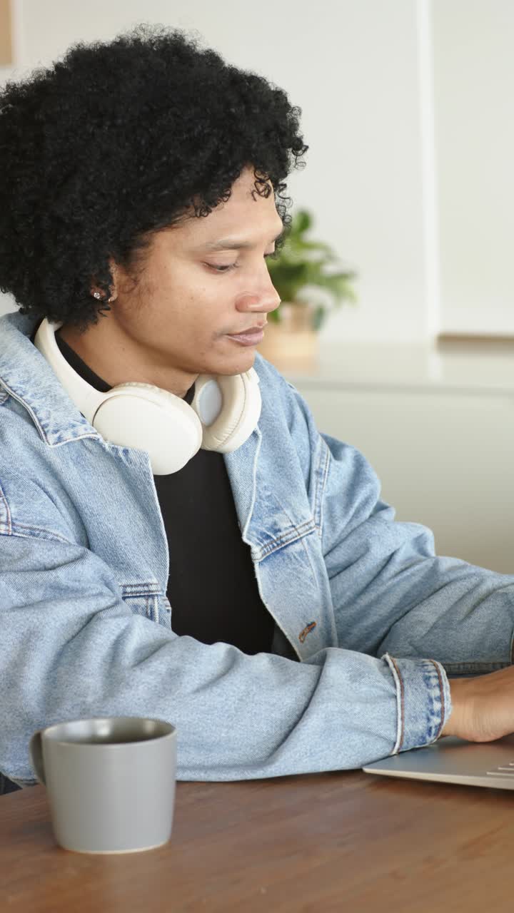 Vertical video: After settling mid adult man at desk typing on laptop with mug finishing tasks