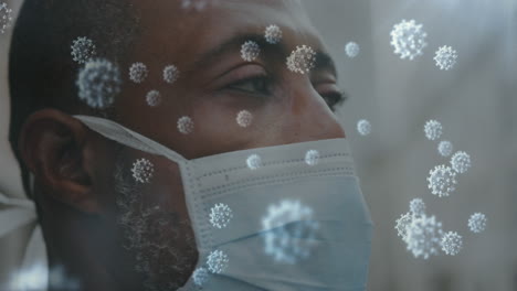 animation of covid 19 cells over close up of african american man wearing face mask