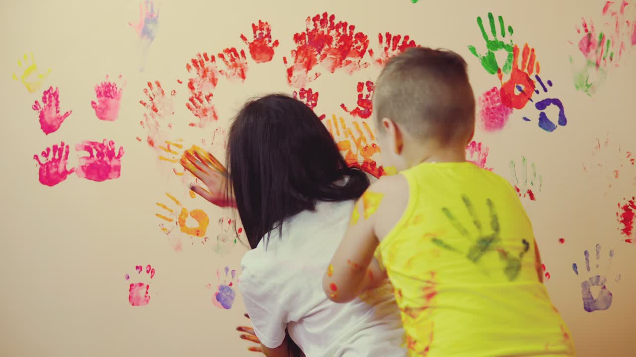 madre feliz y su lindo niño divirtiéndose juntos dejando sus coloridas huellas de manos en la pared y en las camisas. joven familia feliz. concepto de madre e hijo
