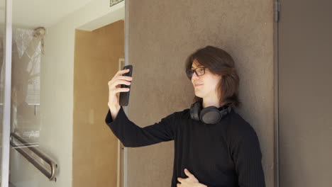 young man with glasses on a video call using his cell phone, headphones around his neck