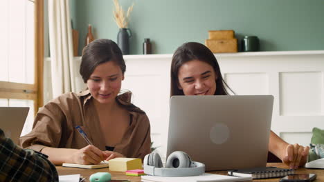 camera focuses on two girls of a study group who are talking and looking at laptop