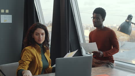 caucasian woman discussing papers with black colleague in office