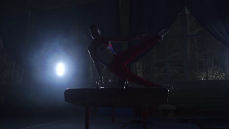 male gymnast performs pommel horse exercise in a dark room in smoke in slow motion. sports for health and achievement