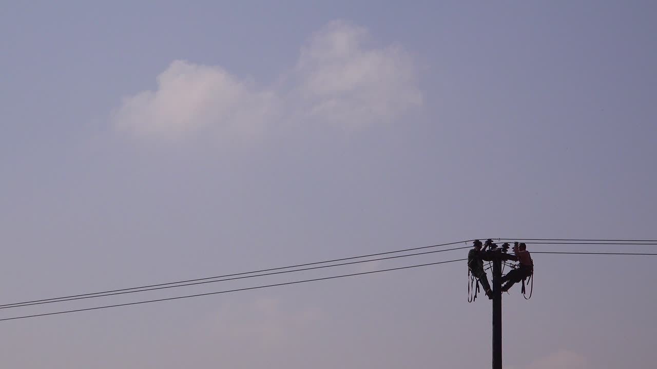 Two men in silhouette work on an electrical cable atop a telephone pole 1