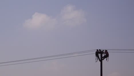 Dos-Hombres-En-Silueta-Trabajan-Sobre-Un-Cable-Eléctrico-Encima-De-Un-Poste-Telefónico-1