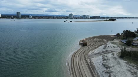 Hochbewegte-Drohnenansicht,-Die-Einem-Großen-Muldenkipper-Folgt,-Der-Sand-Entlang-Einer-Küstenstraße-Am-Strand-Transportiert