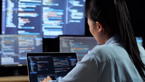 close up back view of asian female programmer thinking about something and raising index finger while writing code by a laptop using multiple monitors showing data on desktops in the office