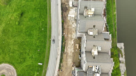 Vista-Aérea-De-Un-Sitio-De-Construcción-Dinámico-Junto-A-Una-Carretera-Bulliciosa,-En-Contraste-Con-Una-Extensión-De-Hierba-Verde