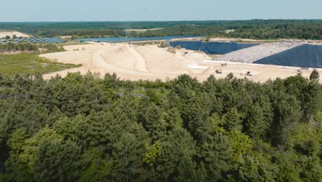 Drone-flight-over-the-forest,-then-discovery-of-a-landfill-site-with-trucks-digging