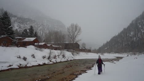 Female-in-snowshoes-walking-by-the-river-on-snow-in-cold-winter-landscape,-Ouray-Colorado-USA,-slow-motion