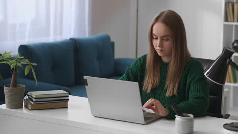 una estudiante está usando una computadora portátil en casa para el aprendizaje electrónico a distancia educación en línea una mujer joven está trabajando con un cuaderno sentada en la mesa en la habitación