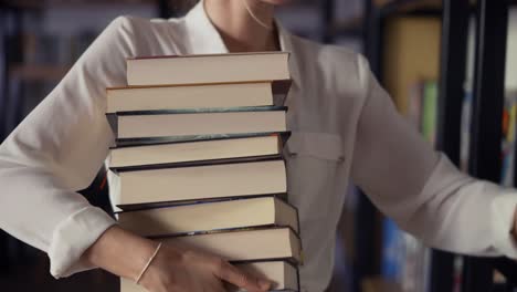 woman holding pile of books in the library, putting more on the stack