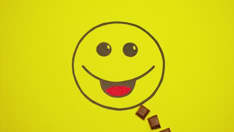 pintado sonriente sobre fondo amarillo. piezas de chocolate se mueven en la boca de sonriente.