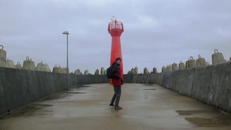 Un-Hombre-Corriendo-Felizmente-Hacia-El-Faro-Rojo,-Llamado-Luz-De-Muelle,-A-La-Entrada-Del-Puerto-De-Kolobrzeg-En-Polonia---Toma-Amplia