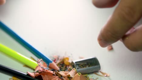 imágenes de manos afilando lentamente un lápiz y algunos lápices de colores con un sacapuntas de cuña