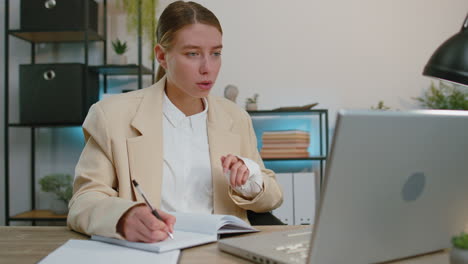 Businesswoman-lawyer-in-suit-working-on-laptop-online,-writing-notes-in-planner-notebook-at-office