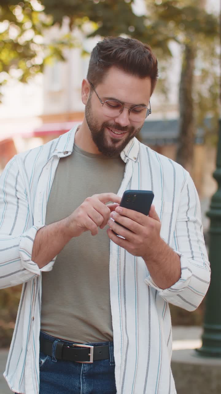 joven sonriente usando su teléfono inteligente escribiendo mensajes de texto desplazando la aplicación de redes sociales en la calle de la ciudad