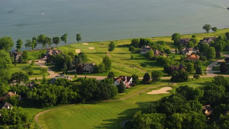 aerial tilt down of golf course along lake como wisconsin with green fields and trees along edge of calm reflective water