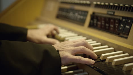 a shot of man's hands playing on the organ, artificial lighting, black and white keys, wooden casing