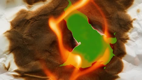 crumpled  white sheet of paper burns with a hole on a green background. original video transition. flame and smoke. green background.