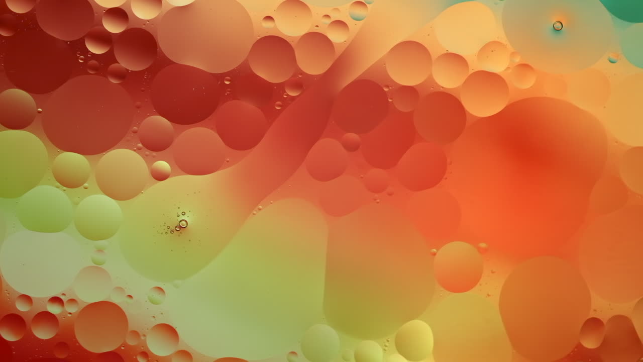 Close-up footage of oil flowing across a water surface with a colourful background