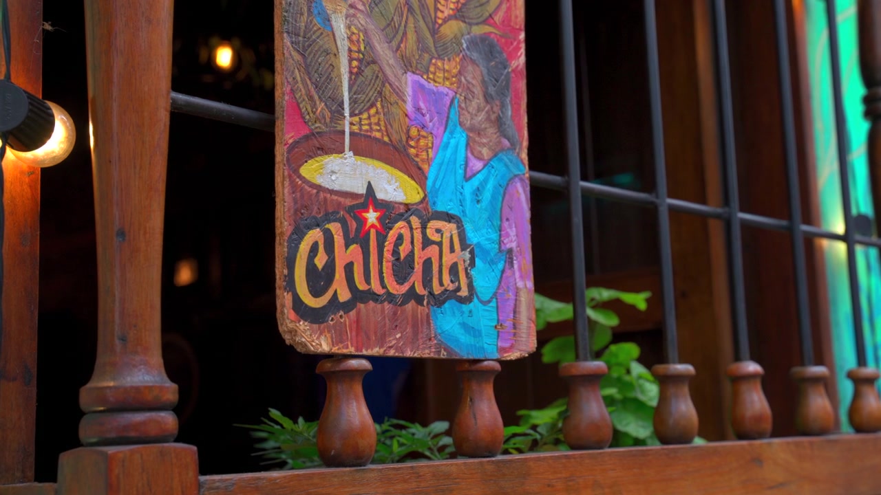 Primo piano statico di un cartello di legno dipinto a mano che pubblicizza la tradizionale bevanda chicha su un balcone di legno a La Candelaria, Bogotà, Colombia.