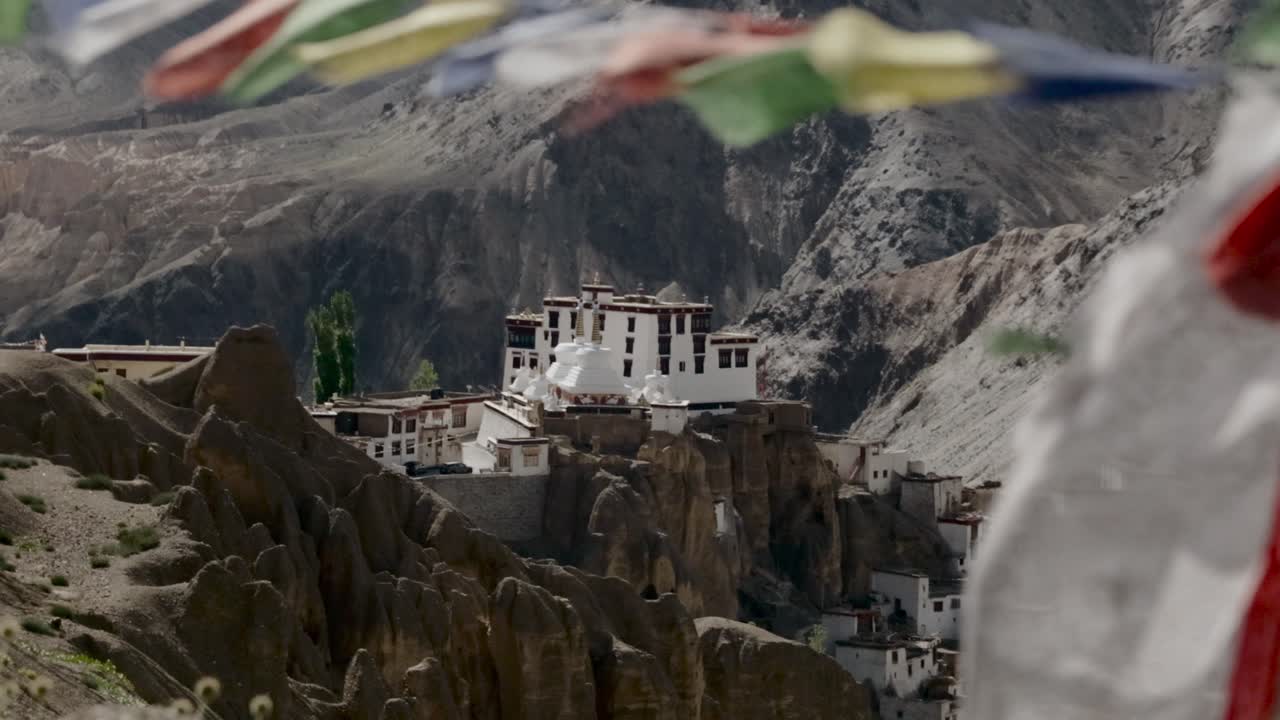 Tibetansk gompa beliggende i et stenet bjerglandskab med farverige bedeflag i slowmotion, der blafrer i en let brise