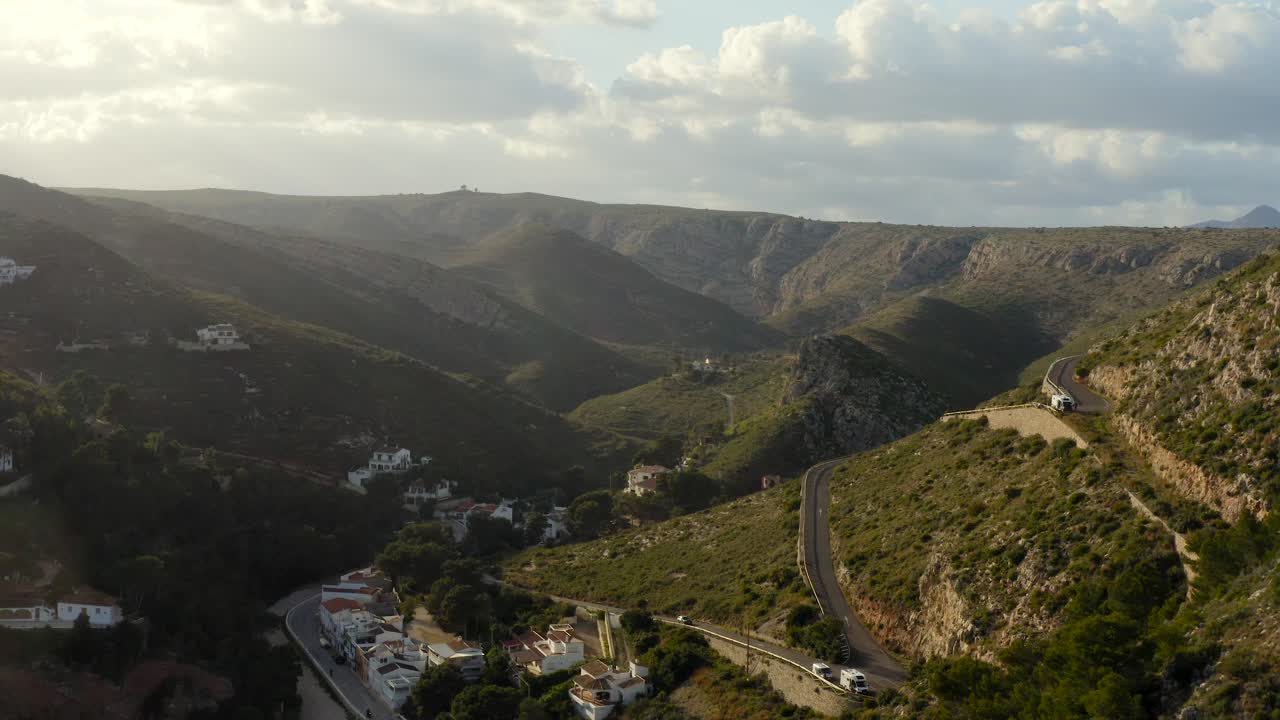 Lunga ripresa aerea che si allontana da strade collinari tortuose e case verso una splendida baia mediterranea azzurra e appartata in Spagna, verso il tramonto
